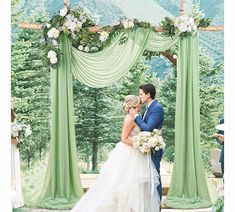 a bride and groom kissing under an outdoor wedding ceremony arch with green draping