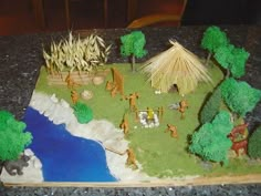 a cake with trees and people on it sitting on a table next to a river