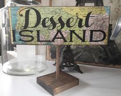 a wooden sign that says desert island on top of a white table next to a glass dome