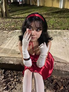 a woman dressed in red sitting on the ground with her hands up to her face