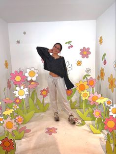 a woman standing in front of a wall with flowers painted on it