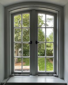 an open window in the corner of a room with grass and trees behind it on a sunny day