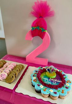 two birthday cakes and cupcakes are displayed on a pink tablecloth with the number 2