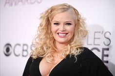 a woman with blonde hair and blue eyes smiling on the red carpet at an awards event