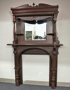 an ornate wooden mantle with mirror above it on carpeted floor next to white wall