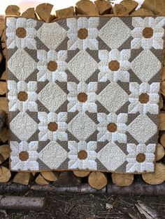 a quilt on top of logs in front of a pile of firewood with brown and white designs