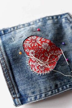 a piece of fabric with some pins sticking out of it sitting on top of a pair of jeans