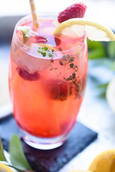 a close up of a drink in a glass with lemons and raspberries