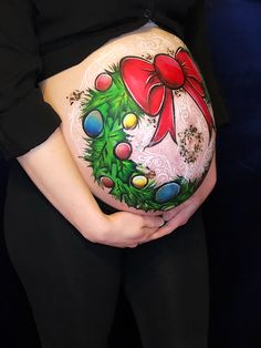 a pregnant woman holding her belly decorated with christmas wreaths and bows, while wearing black tights