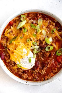 a white bowl filled with chili, cheese and sour cream on top of a table