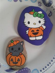 two rocks decorated with hello kitty and pumpkins on a white plate next to each other