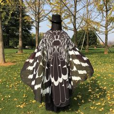 a man in a black and white costume standing on grass with trees behind him wearing a top hat