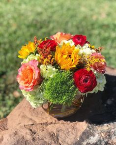 a vase filled with lots of colorful flowers on top of a stone slab in the grass