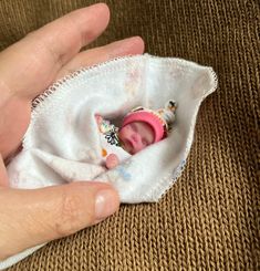 a hand holding a tiny baby doll in a cloth bag