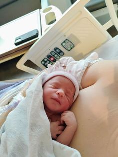 a baby laying on top of a bed under a blanket next to an electronic device