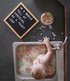 a baby in a bath tub with sprinkles on the floor next to it