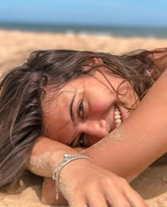 a woman laying in the sand with her arm around her head and hand on her chest