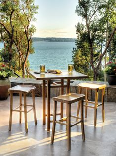 three wooden stools sit at a table overlooking the water