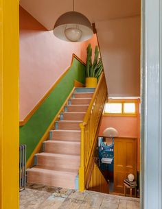 the stairs are painted bright pink, green and yellow in this entryway with potted plants on either side