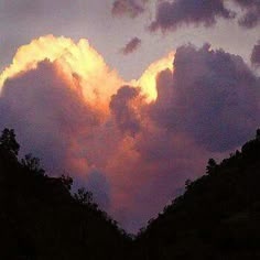 the sun is setting behind some clouds in the sky above trees and mountains, with dark shadows on them