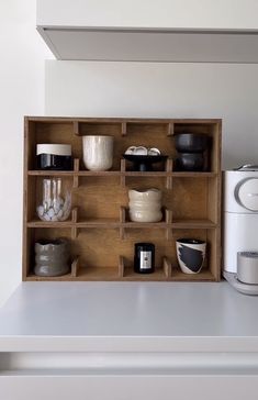 a wooden shelf filled with bowls and cups on top of a white counter next to a coffee maker