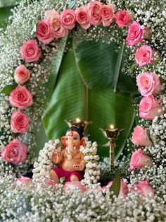 there is a small statue in the middle of flowers with candles on each side and an elephant figurine behind it