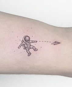 a small tattoo on the arm of a person wearing an astronaut suit and flying a paper airplane