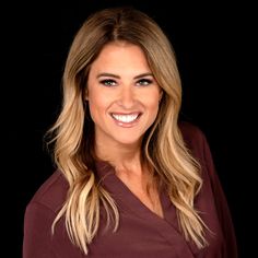 a woman with long blonde hair smiling at the camera while wearing a maroon shirt and black pants