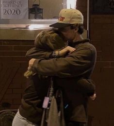 two people hugging each other in front of a store window with signs on the wall