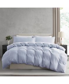 a bed with blue comforter and pillows in a gray room next to a window