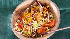 a wooden bowl filled with salad on top of a green table cloth next to two spoons