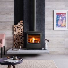 a wood burning stove in a living room next to a pile of firewood and pink chairs