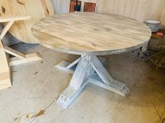 a round wooden table sitting on top of a floor next to a pile of wood