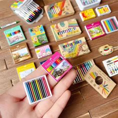 a person is holding some colorful crayons in their hand and there are many different ones on the table