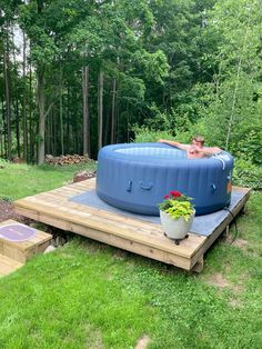 a man laying in an above ground hot tub on a wooden platform next to some trees