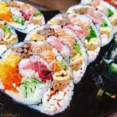 several sushi rolls with various toppings on top of them sitting on a black plate