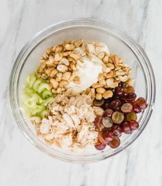 grapes, nuts and chicken in a glass bowl on a marble countertop with white background