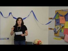 a woman standing in front of a whiteboard with blue ribbon on it and another person holding a piece of paper