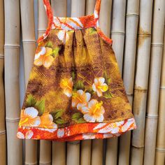 a brown and orange floral dress hanging on a bamboo wall next to the bamboo fence