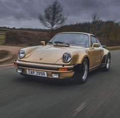 an old yellow porsche is driving down the road