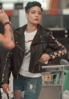 a woman with green hair wearing a black leather jacket and holding a shopping cart in her hand