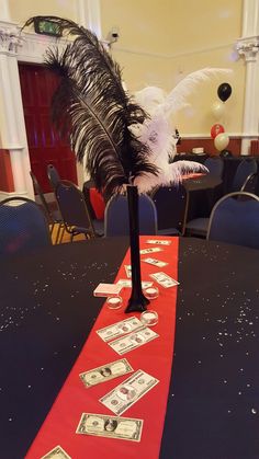 a red table runner with money on it and a feather centerpiece in the middle