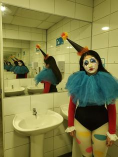 a woman with clown makeup standing in front of a bathroom mirror wearing a blue and orange costume