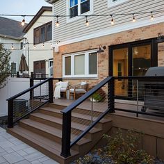 an outdoor deck with patio furniture and string lights strung over the railings, leading to a back yard