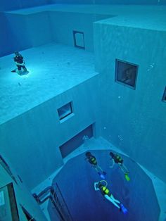 two people in scuba gear are swimming through an underwater pool with blue water and white walls