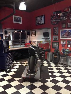 a garage with black and white checkered flooring, red walls and motorcycles on the wall