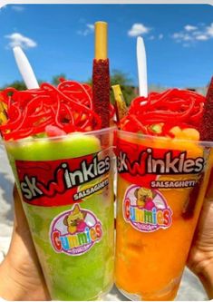 two people holding up drinks with strawberries and oranges in them on the beach