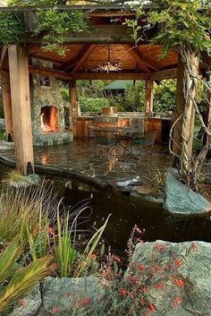 an outdoor gazebo with a table and chairs next to a small pond surrounded by rocks