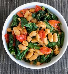 a white bowl filled with spinach and chickpeas on top of a table