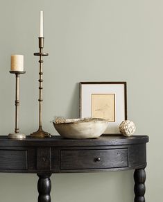 a wooden table with a bowl and two candles on it next to a framed photograph